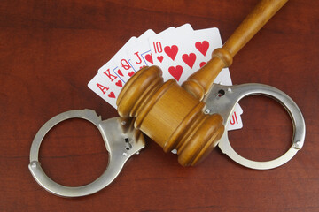 Five hearts playing cards, handcuffs and judge gavel on wooden table. Court and gambling concept.