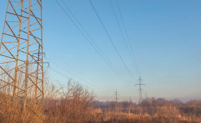power line pylons in autumn field with trees at dawn