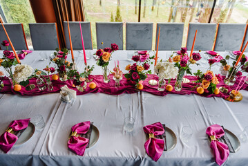 Luxury elegant table setting dinner with floral centerpiece in a restaurant. Decoration with orange flowers roses, candles, fruits. Plate, glasses, forks, pink napkins. Decor rustic style. Top view - Powered by Adobe