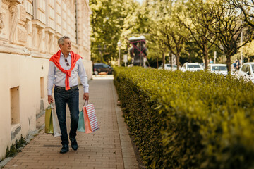 Fototapeta na wymiar Cheerful elegant dressed senior man walking with a shopping bags in the city.