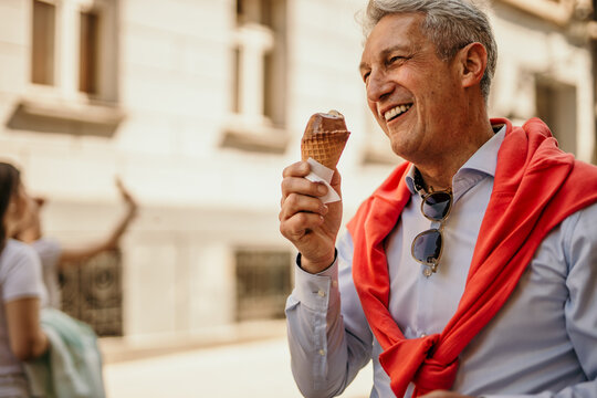 Senior man elegantly dressed eating ice cream on a sunny day in the city.