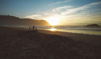 Silhouettes of happy unrecognizable children playing on background of beach at sunset