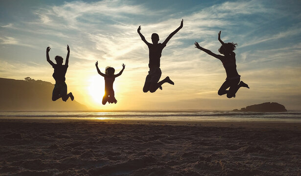 Silhouettes of happy unrecognizable children jumping in the beach at sunset