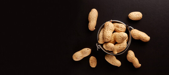 Fototapeta na wymiar Unshelled peanuts in a small metal bucket on a black background.