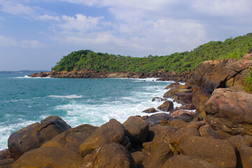Dark rocks in the sun at Jungle Beach, Unawatuna, Sri Lanka, blue sky with clouds, copy space for text