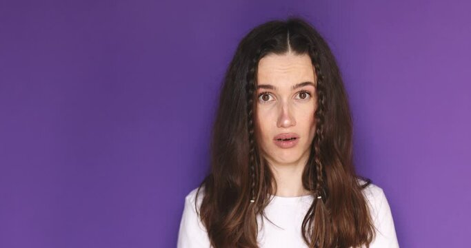 Young brunette woman with braids waves finger saying no to suggestions. Confident girl shows stop gesture standing isolated on purple background. 