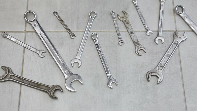  Open-end wrenches and box wrenches of various sizes lie on the ceramic floor. A man picks up wrenches from the floor.
