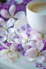 Delicate spring flowers of lilac and jasmine and a cup of coffee with milk. Delicate morning coffee with a wonderful spring-summer mood. Soft selective artistic focus.
