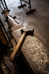 Hammer, anvil and blacksmith workplace in a iron factory and industrial workshop. Tools, metal work and steel artisan bench with craftmanship equipment to forge in warehouse with metals and materials
