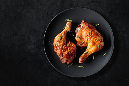 Grilled chicken drumsticks with rosemary on a black stone table.