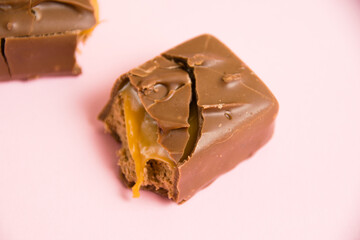 Pieces of a chocolate bar with caramel macro on a pink background