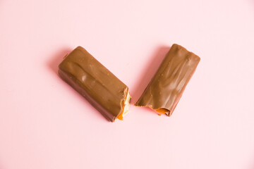 Flatlay, appetizing pieces of chocolate bar with caramel close-up on pink background