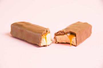 Pieces of appetizing chocolate bar with caramel and nougat macro on a pink background