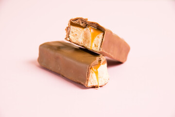 Pieces of appetizing chocolate bar with caramel and nougat macro on a pink background