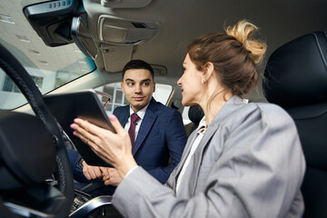 Woman showing tablet to businessman sitting in car