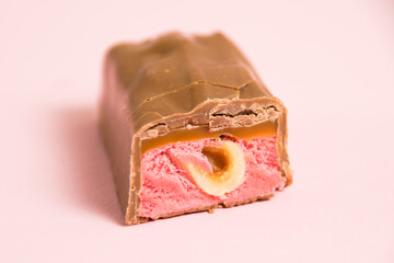 Pieces of appetizing chocolate bar with whole nut and strawberry on a pink background