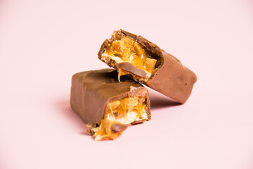 Pieces of delicious chocolate bar with nougat, caramel and peanuts on a pink background