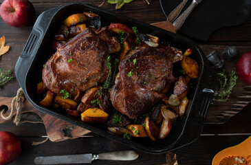 Meat dish for thanksgiving with roasted turkey shanks. Served with butternut pumkin, red apples, onions in roasting pan on rustic and wooden table background