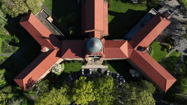 An aerial view of a large Catholic seminary on Long Island, NY on a sunny day. Surrounded by green trees and grass. The drone camera tilted down, dolly out and tilt up to reveal the entire structure.