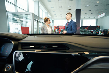 Man and woman in suits talking in car dealership