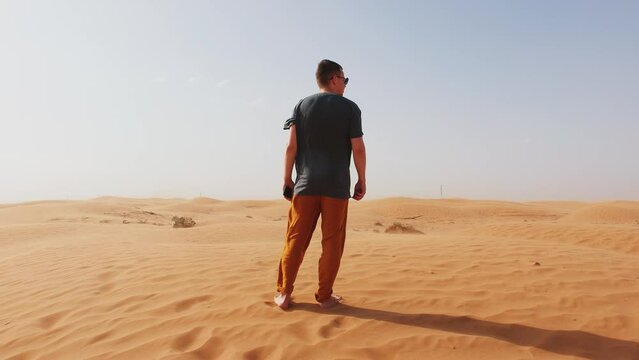 Barefoot young man stands in desert and looks around. Back view. Concept of relaxation and contemplation. Slow motion