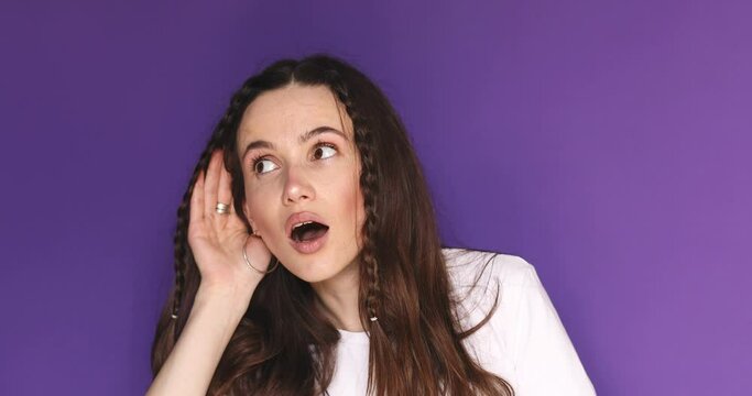 Curious nosy funny young woman brunette hair try to hear you overhear listening intently hot news isolated on purple color wall background studio portrait. Girl try to hear you with hand at ear.