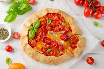 Tomatoes galette or pie with cheese and herbs on a white wooden background. Vegetarian dish. Selective focus.