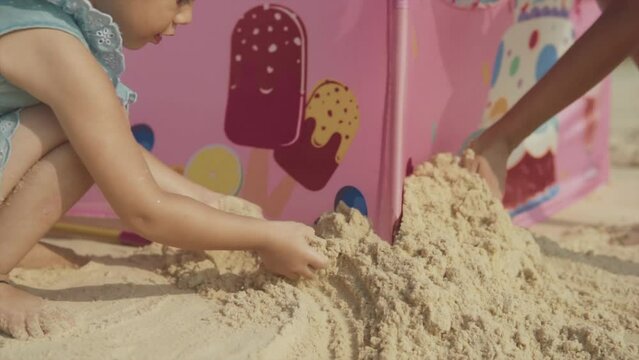 Close up of parent and daughter playing with sand pushing it against pop up tent