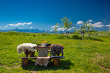 Bacówka na Rusińskim Wierchu i okolice. Góralskie futra na stole na tle zielonych pól i błękitnego nieba. 