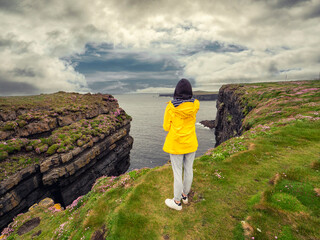 Teenager girl in yellow jacket on edge of stunning cliff in county Clare, Ireland, Loop head area....