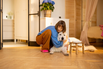 Portrait of young woman with her huge white dog, hugging together at home. Concept of domestic lifestyle and friendship with pets. Maremma shepherd dog