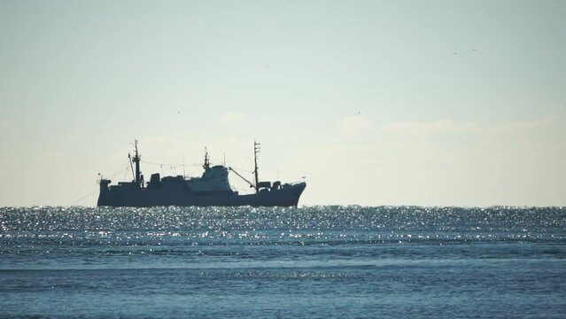 Silhouette of fishing ship in the sea on horizon. Ship sailing in the sea. Small waves on the golden surface of warm water with bokeh lights from the sun. Sea, nature and outdoor travel.