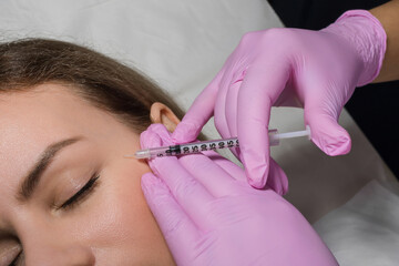 Beautiful young woman is getting an injection in her face and smiling, lying with closed eyes