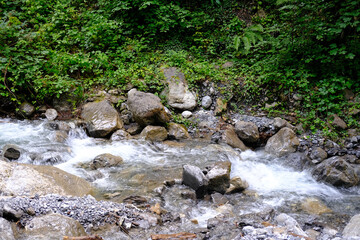 powerful stream of clean water quickly flows along mountain river, splashes scatter from stones, concept of wild nature, symbol of natural resources, alternative energy, water sports