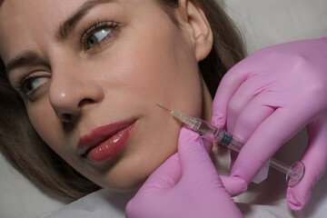 Attractive young woman is getting a rejuvenating facial injections. She is sitting calmly at...