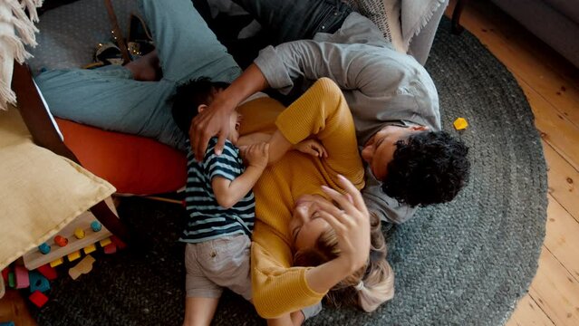 Son having fun with his parents in a playful moment, he laughs and enjoys himself as they tickle all over his body. Little boy enjoying the love and affection from his mother and father at home. 