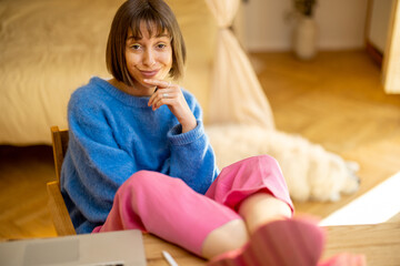 Portrait of young woman in colorful casual clothes sitting relaxed by the table at cozy home atmosphere. Concept of home office and remote work