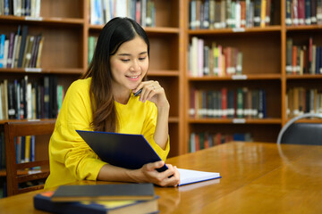 Beautiful asian woman sitting in library and reading text book during preparing for exam. Education concept