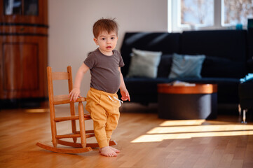 Little toddler boy sitting on wooden rocking chair in living room with dark sofa