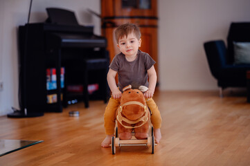 Little happy toddler boy in t-shirt riding brown toy horse