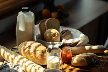 Baked bread and glass of milk on wooden table in kitchen with sunlight from window. Healthy eating and traditional bakery concept