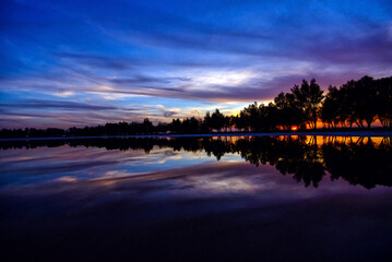 Cloud formations in beautiful colors and their reflections on the surface of the water in the lake as if it were a wonderful plastic painting with the presence of trees at sunset and Background image 