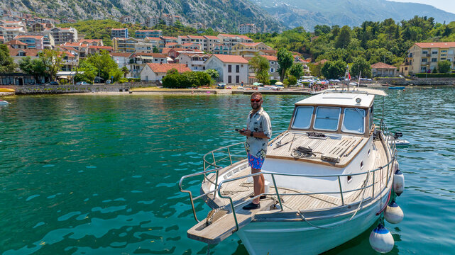 man on boat with drone remote controller taking a picture with kotor city shore on background
