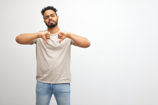 Young african american man male wearing t-shirt standing over isolated white background looking unhappy and angry showing rejection and negative with thumbs down gesture. Bad expression.