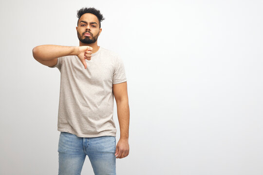 Young african american man wearing t-shirt standing over isolated white background looking unhappy and angry showing rejection and negative with thumbs down gesture. Bad expression.