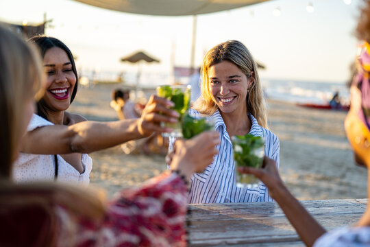 Happy Girls Having Fun Drinking Cocktails At Bar On The Beach, Summer Lifestyle And Travel Concept, Celebratory Toasting Moment