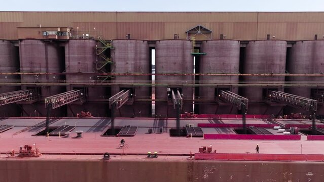 Workers supervising taconite iron loading into haul of large freight ship at ore dock in Wisconsin