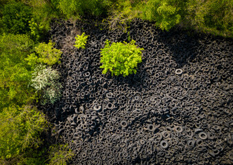 Aerial view of the stark contrast between a massive landfill of used car tires and the surrounding...
