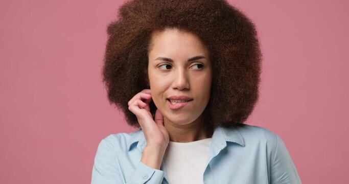 Pensive young arican american woman with curly hair thinking and smiling standing over pink studio background