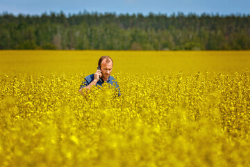 Naklejka na ściany i meble Agronomist man inspects rapeseed crops. Increasing yields and organic food production. Application of new technologies in agriculture.